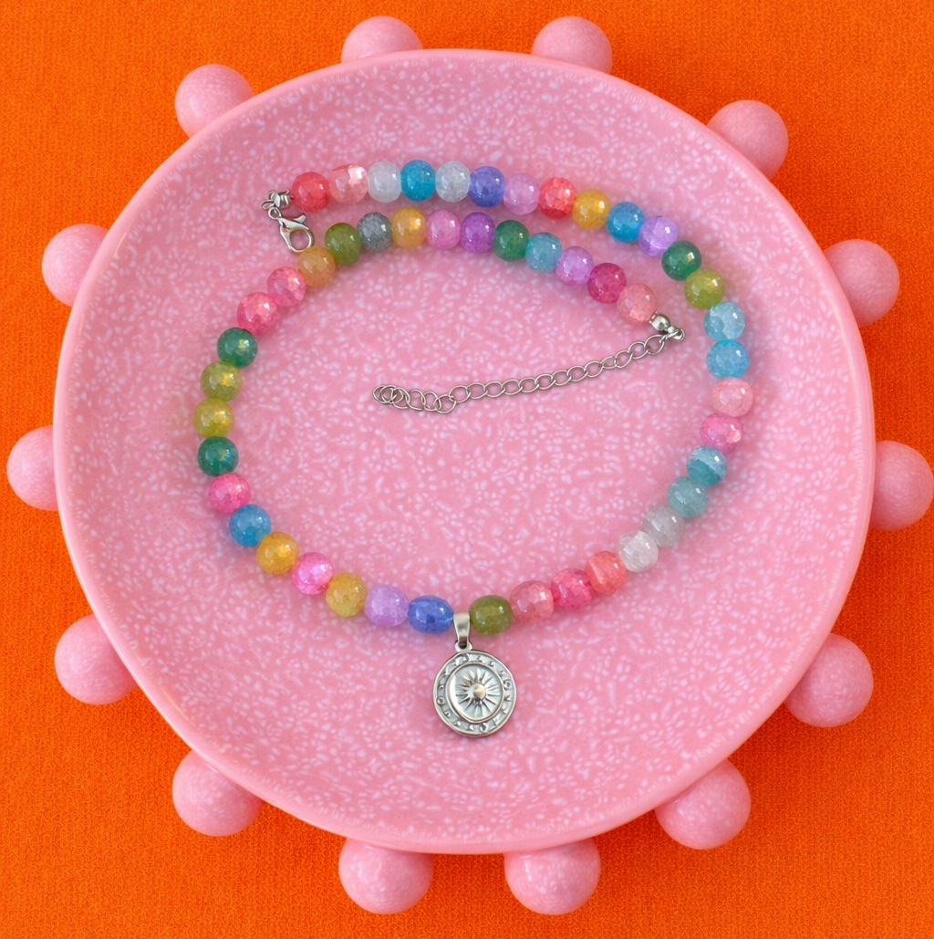 Colorful beaded necklace with a pendant on a pink stand against an orange background